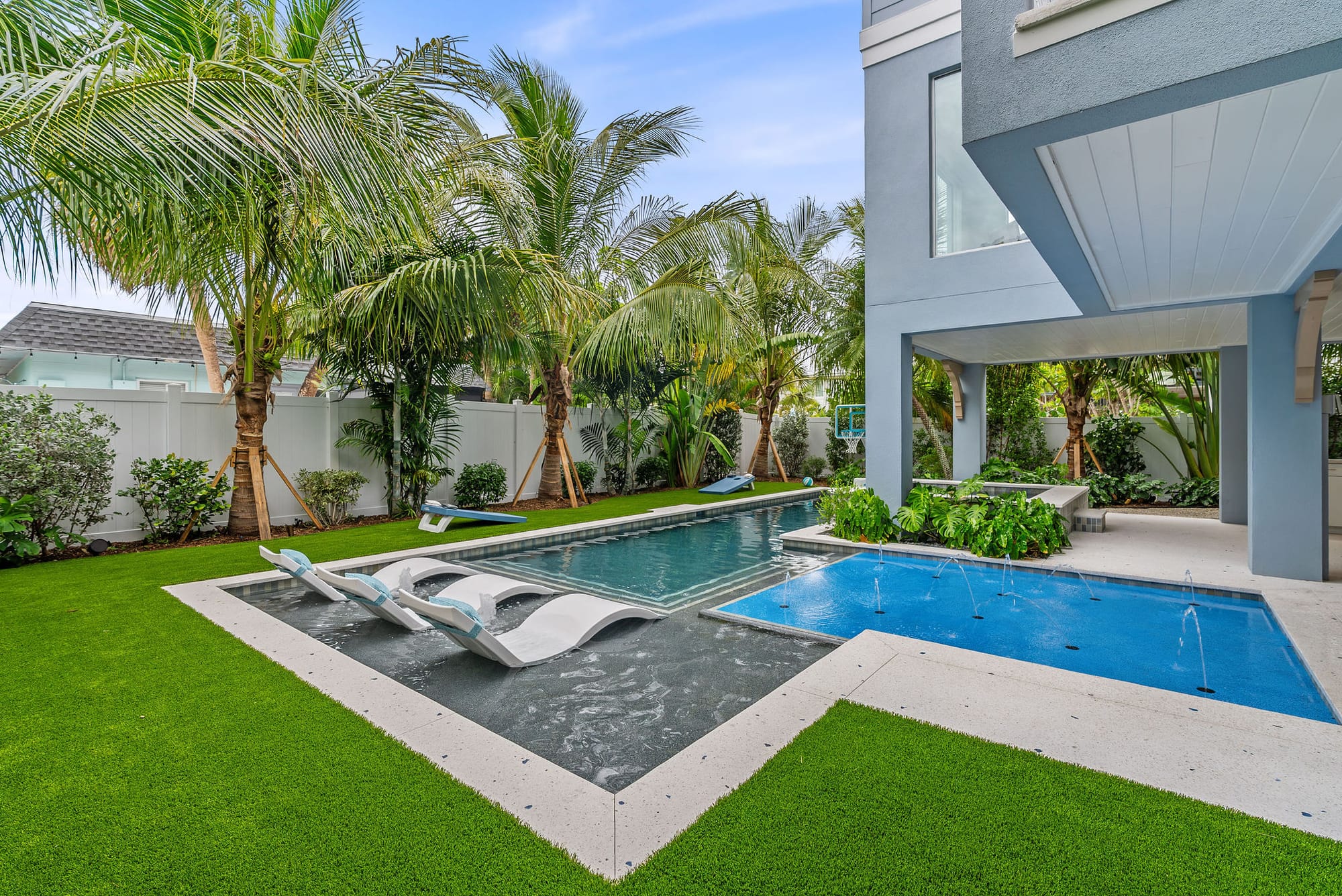 A geometric custom pool with tanning ledge loungers and a deck-jet splash pool framed by tropical palms.