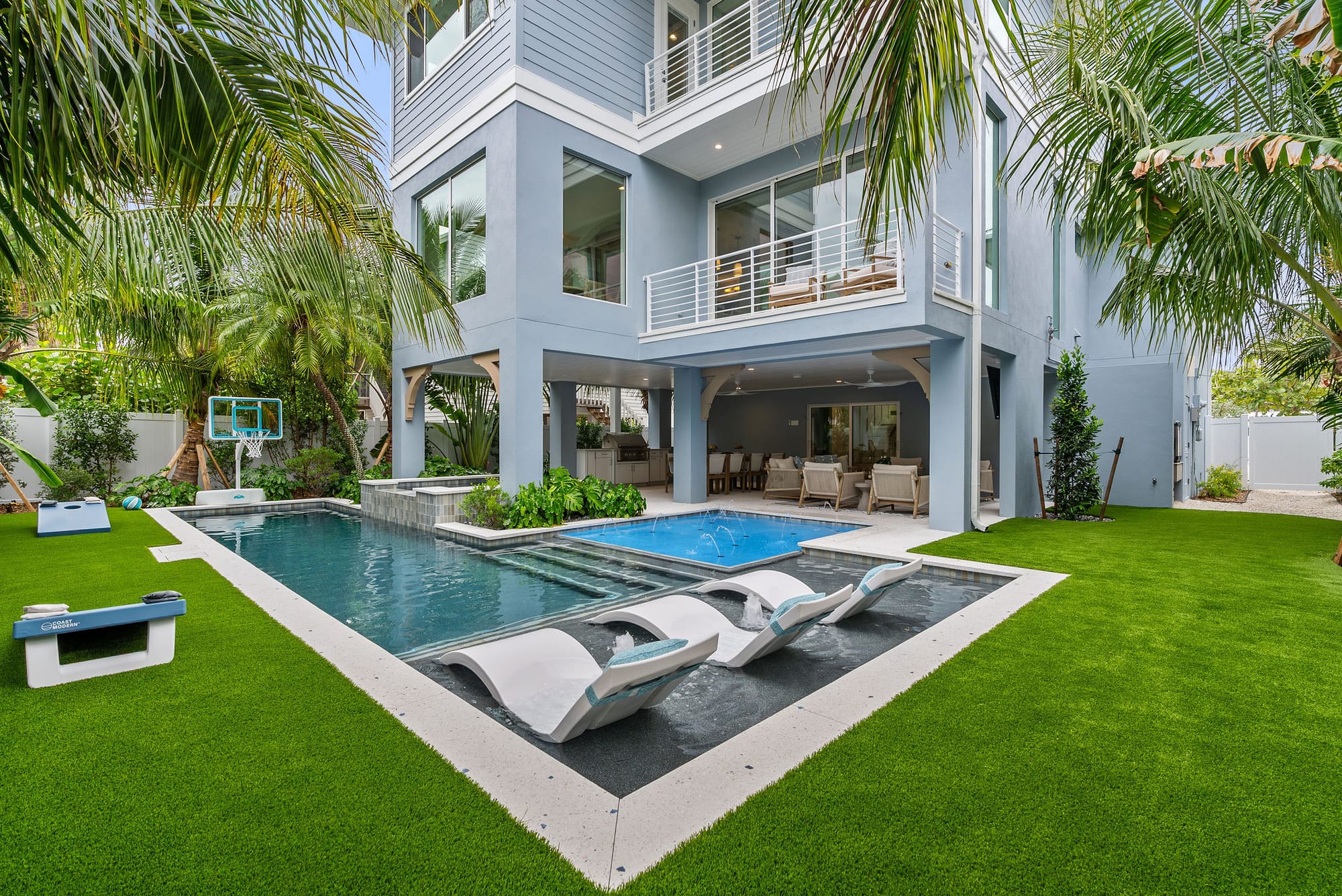 A custom pool and green lawn leading to the covered outdoor living area of a coastal home in Holmes Beach, FL.