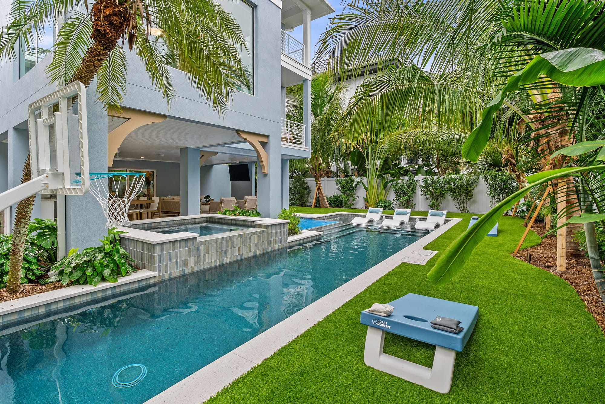 A long custom pool beside a tiled raised spa with lush tropical landscaping along the lawn.