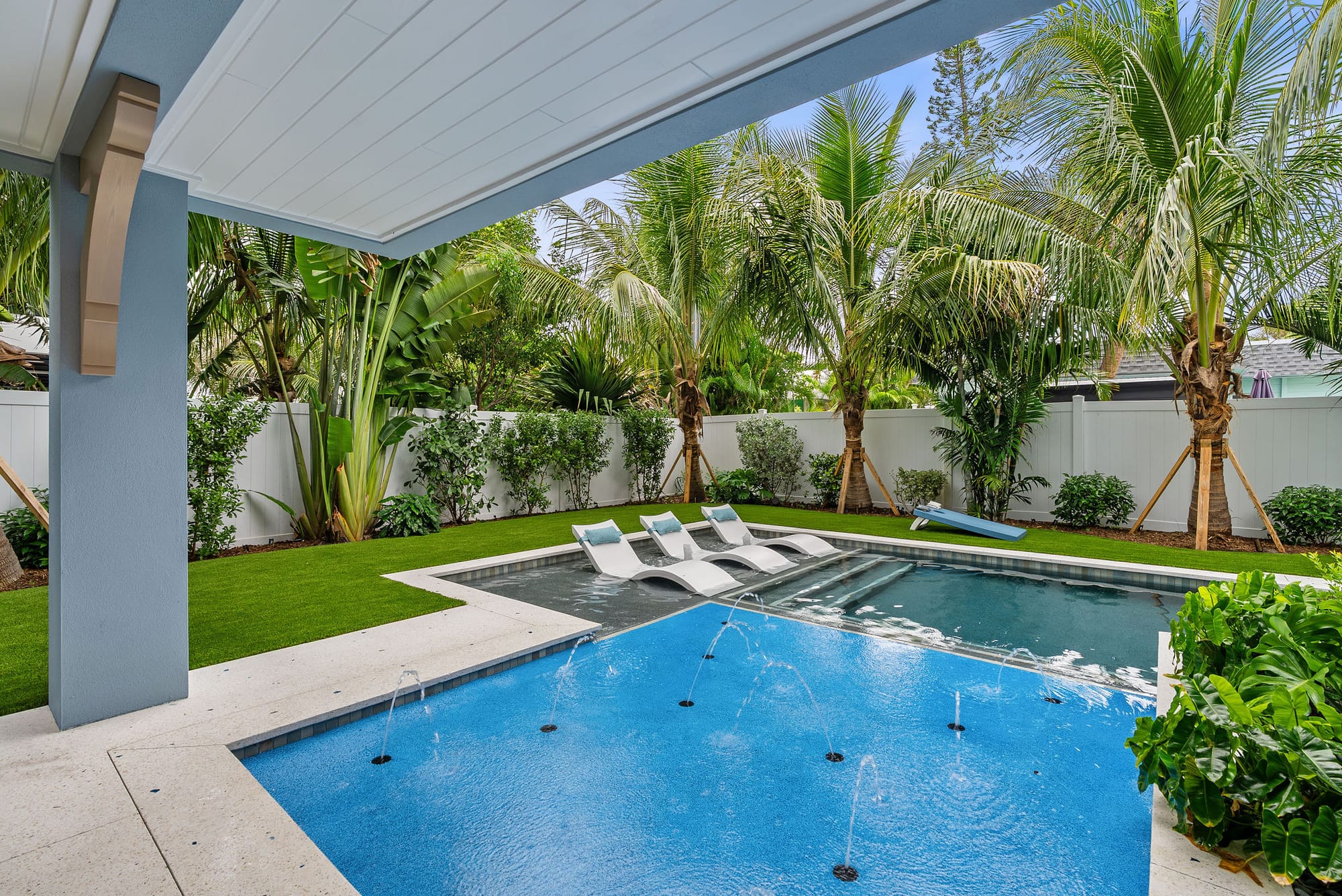 Deck jets arcing into a shallow splash pool, viewed from beneath the covered lanai.