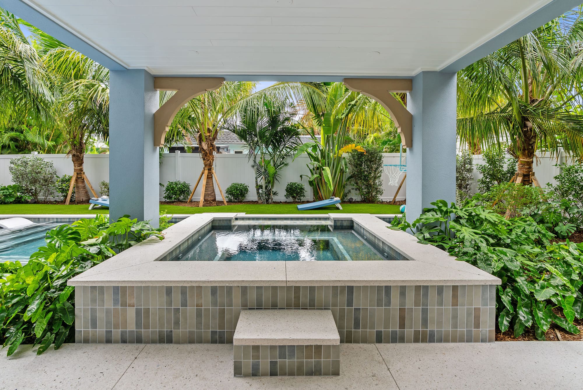 A raised spa finished in blue-gray tile with white coping, framed by lanai brackets and tropical plantings.