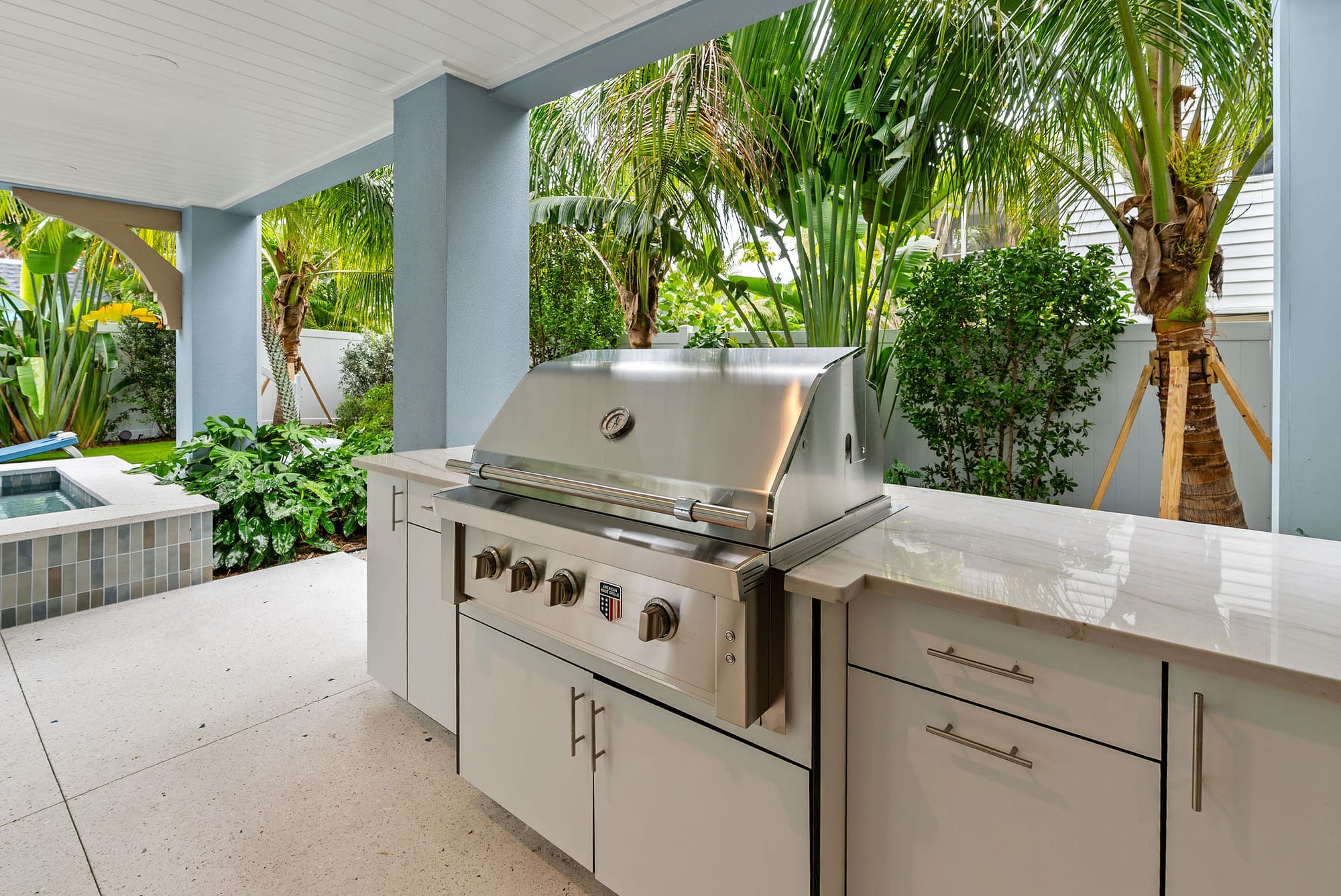 An outdoor kitchen with a built-in stainless steel grill and stone countertops under the covered lanai.