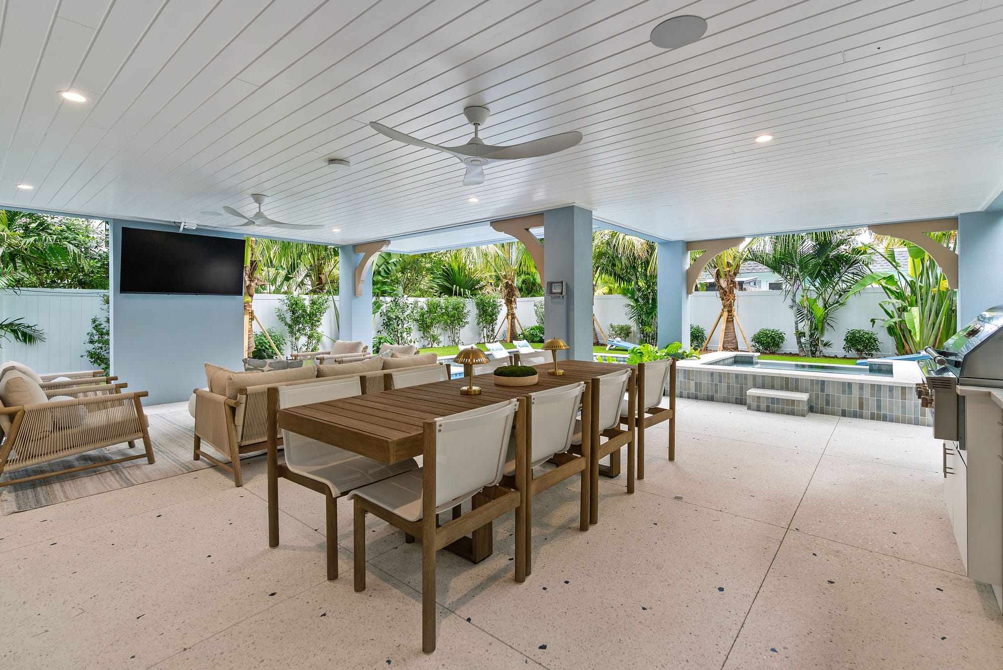 A covered lanai with outdoor dining, lounge seating, and a TV overlooking the pool and spa.