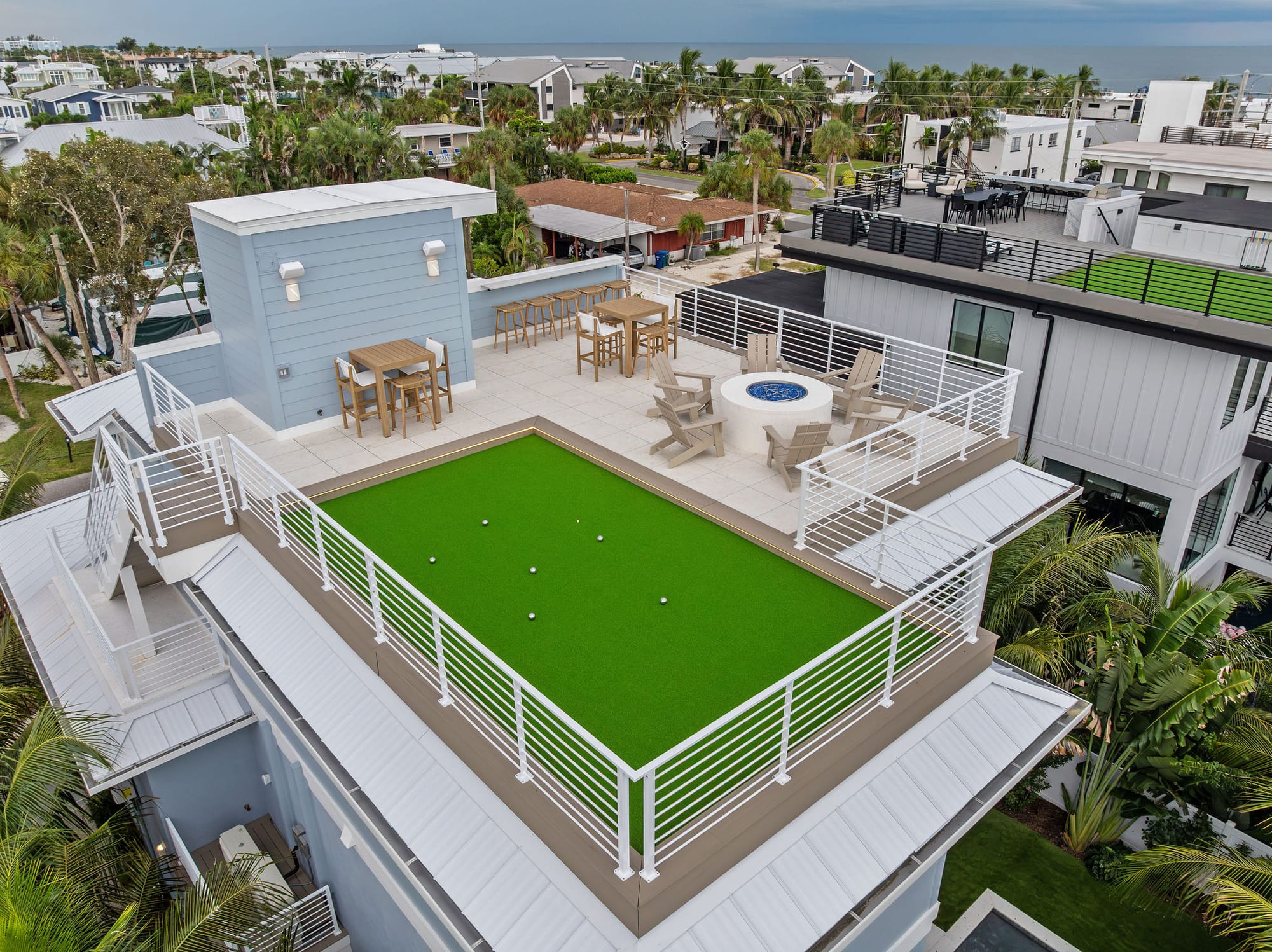 An aerial view of a rooftop deck with a putting green, fire pit, and bar-height seating in Holmes Beach, FL.