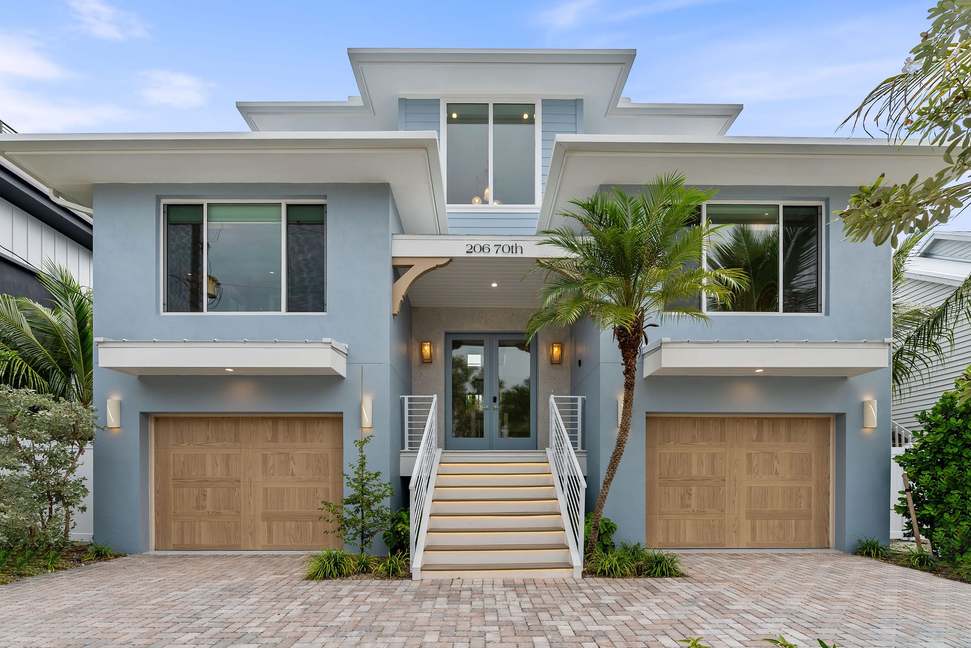 The front of 206 70th Street with a paver driveway, lit entry stairs, and palm landscaping.