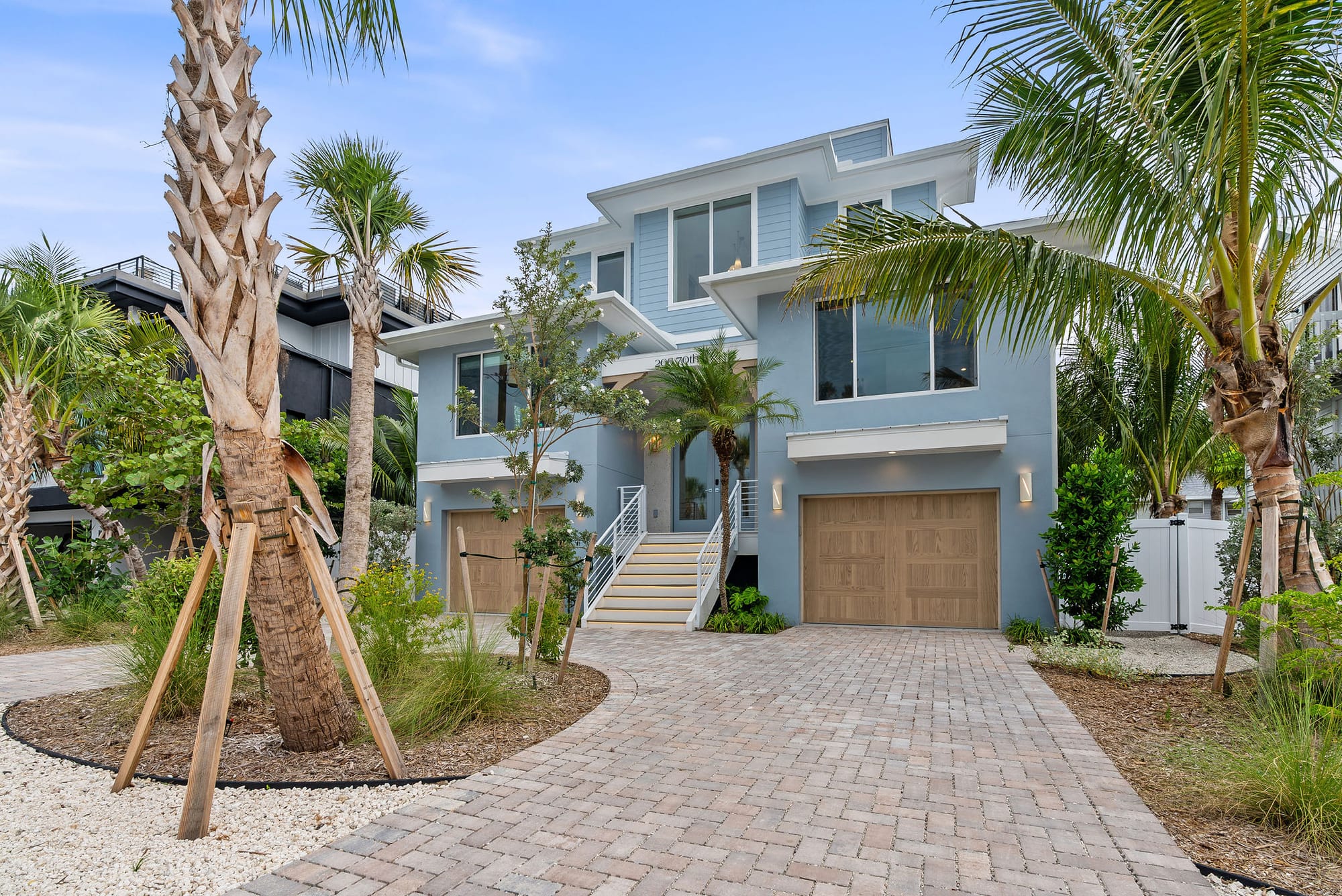 A paver driveway lined with tropical front landscaping, palms, and shell mulch beds.